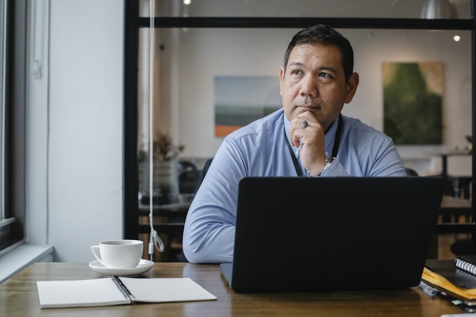 A businessman deep in thought while working on a laptop in a modern office setting.